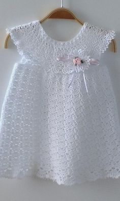 a white crochet dress with pink flowers on the front and back, hanging from a wooden hanger