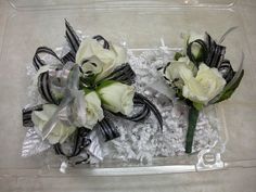 two white roses in a clear box with black ribbon and silver sequins on it