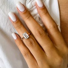 a woman's hand with an engagement ring on her finger and white manicured nails