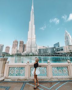 a woman standing on a bridge looking at the burjt in the background