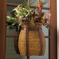 a basket hanging from the side of a door with flowers in it and leaves on top