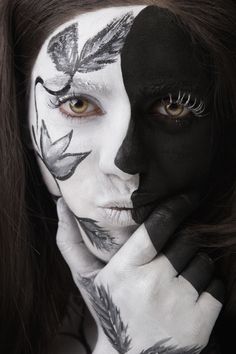 a woman with black and white face paint holding her hand to her face while looking at the camera