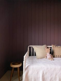 a white bed sitting next to a wooden stool and wall with purple paint on it