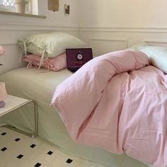 a laptop computer sitting on top of a bed next to pink sheets and pillow cases