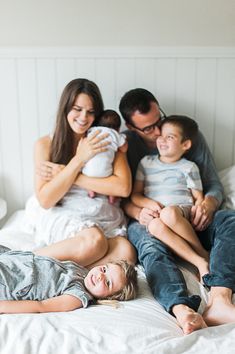 a family is laying on the bed with their arms around each other and smiling at the camera