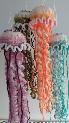 three crocheted jellyfishs hanging from strings on a shelf in front of a white wall