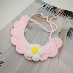 a crocheted pink and white necklace with a flower on the front, sitting on top of a magazine