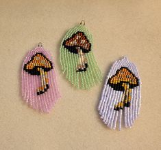 three beaded earrings with mushrooms on them sitting on a counter top next to each other