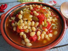 a bowl filled with beans and vegetables on top of a wooden table next to a spoon