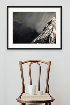 a chair with two cups on it in front of a wall mounted art print that has a snowy mountain