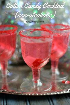 three glasses filled with red liquid sitting on top of a metal tray next to a christmas tree