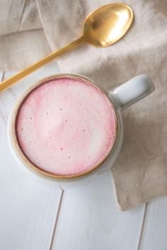 there is a cup with pink liquid in it next to a spoon