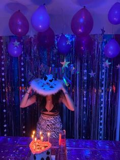 a woman standing in front of a birthday cake with candles on it and decorations around her