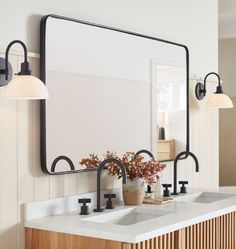 a bathroom vanity with two sinks and a large mirror above it, in front of a white wall