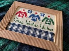 a cross stitched picture frame with some sweaters on it and the words cozy winter wishes