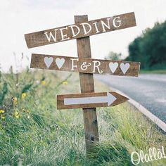 a wooden sign that says wedding and hearts on it sitting in the grass next to a road