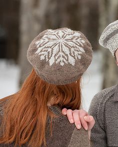 two people standing next to each other in the snow wearing knitted hats and scarves