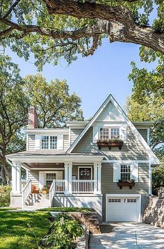 a gray house with white trim and two car garages on the front porch is surrounded by trees