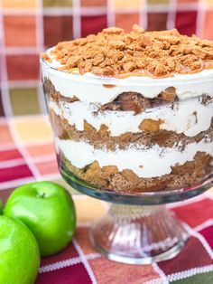 an apple dessert with white frosting and crumbs on top, sitting next to two green apples