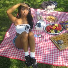 a woman sitting on top of a picnic blanket next to a plate of fruit and waffles