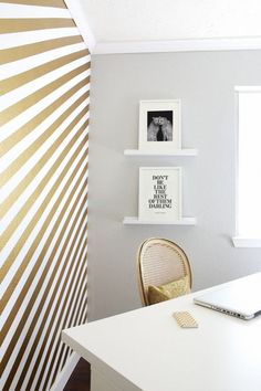 a laptop computer sitting on top of a white desk next to a wall with gold stripes