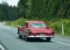 an old red car driving down the road