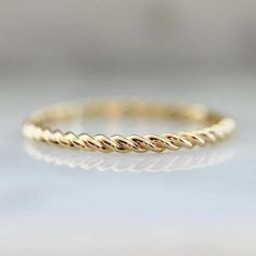 a yellow gold wedding band with twisted rope design on the side, sitting on a white surface