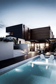 an outdoor swimming pool in front of a modern house at dusk with people sitting on the deck