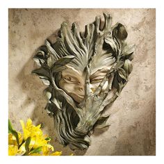 a sculpture of a woman's face with leaves and flowers in front of it