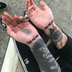 a person sitting on the ground with their hands crossed out and tattoos on both arms