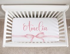 a white crib with a pink bow and name on the pillow that says amelie