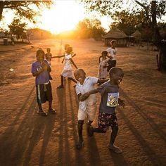 several children are playing in the dirt with their arms around each other as the sun sets