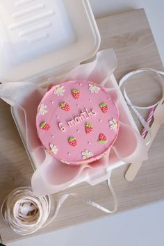 a pink cake with strawberries on it sitting in a box next to some scissors