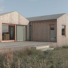 a wooden house sitting on top of a grass covered field next to a building with sliding glass doors