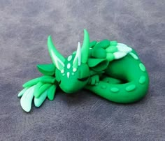 a green and white dragon figurine laying on top of a gray surface with it's eyes closed