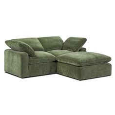 a green sectional sofa with pillows on it's back and foot rest in the middle