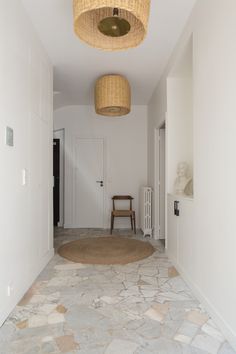 an empty hallway with a round rug on the floor and two wicker lamps hanging from the ceiling