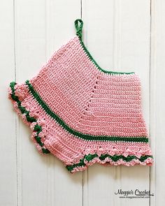 a crocheted pink and green top hanging on a white wooden wall next to a pair of scissors