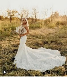 a woman in a wedding dress standing in the middle of a field holding a bouquet