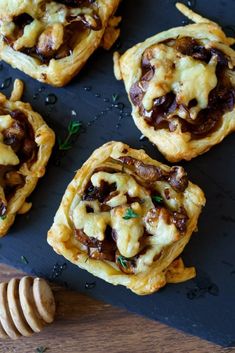 small pastries with meat and cheese are on a black plate next to a honey comb