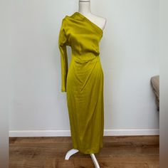 a mannequin wearing a green dress in front of a white wall and wooden floor