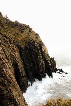 an ocean cliff with waves crashing into the shore and grass growing on it's sides