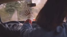 a woman driving a car while holding her hand up to the sunroof window