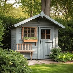 a small blue shed with a wooden bench in the front yard and trees around it