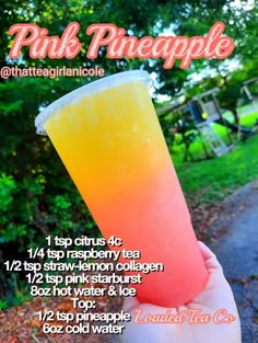 a hand holding up a pink pineapple drink in front of some trees and grass