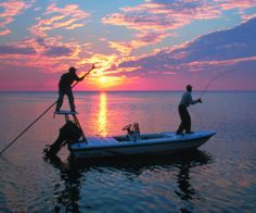 two men are fishing in the ocean at sunset with their boat on the water and one man is holding a rod