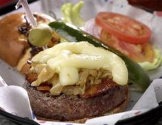 a close up of a hamburger with cheese and onions on the top, next to a pickle