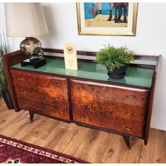 a wooden dresser with green glass top and two potted plants on the bottom shelf