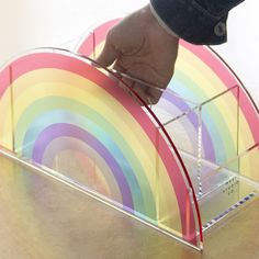 a hand is touching the bottom of a clear box with a rainbow design on it