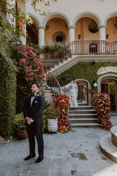 a man in a tuxedo standing next to some flowers on the steps and stairs